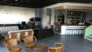 Un espace détente comprenant un canapé, plusieurs fauteuils en osier, un bar avec un comptoir et des étagères remplies de bouteilles, et un téléviseur.
