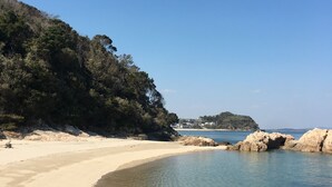 Une plage à l’eau claire, avec un rivage sablonneux et des affleurements rocheux.