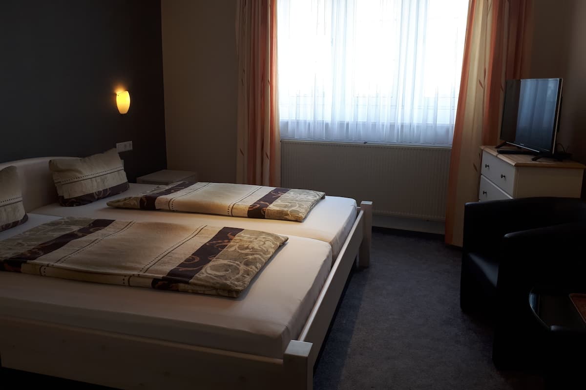 Une chambre d’hôtel avec deux lits, un bureau, une chaise, une télévision et une fenêtre avec des rideaux.