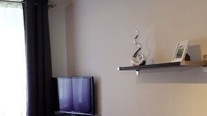 A modern living room with a flat-screen TV mounted on the wall, a black leather sofa, a small table with a glass, and a decorative item on a shelf. - Pension Elisabeth (Cochem)