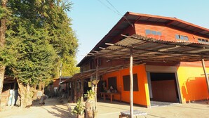 A rustic building with a red roof and orange walls, featuring a covered outdoor seating area and a visible entrance. - Ram Yai Homestay - Hostel (Sukhothai)