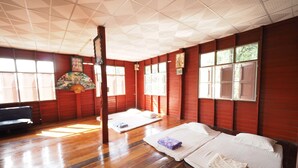 A room with wooden floors, a bed with white bedding, a sofa, and a large window with a view of trees. - Ram Yai Homestay - Hostel (Sukhothai)