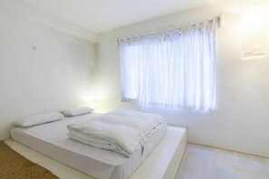 Ein Schlafzimmer mit Bett, einem Fenster mit Vorhängen und einer Lampe.