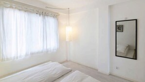 A minimalist bedroom with a large window, a bedside lamp, and a mirror on the wall. - Four Red Doors Apartments (Kathmandu)
