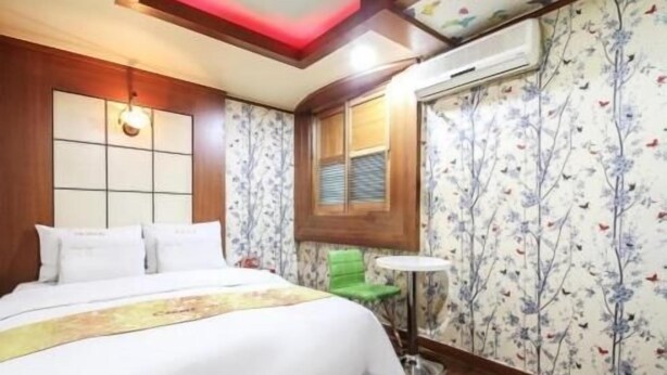 A hotel room with a bed, a small table, and a window with floral wallpaper. - Couple Motel (Seoul)