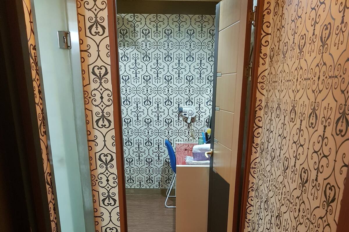 A narrow hallway with patterned wallpaper, leading to a room with a tiled floor and a blue chair.