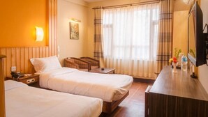Habitación de hotel con dos camas, un escritorio, una silla, un televisor y una ventana con cortinas.