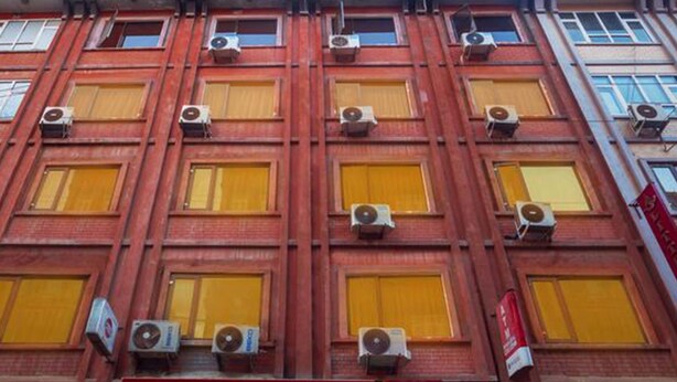 Un edificio de varios pisos con fachada roja, varias unidades de aire acondicionado y ventanas amarillas.
