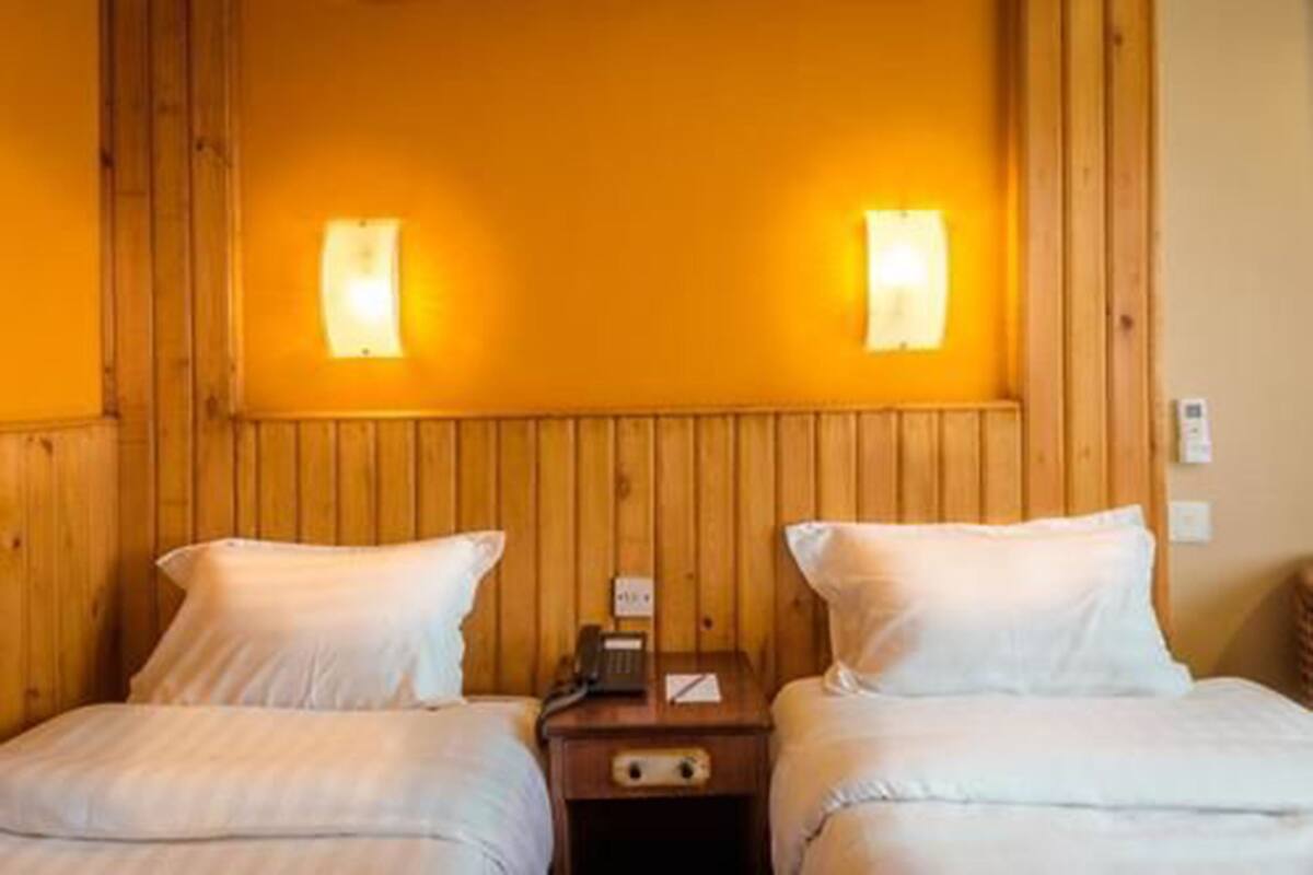 A room with two beds, wooden paneling, and a nightstand with a phone.