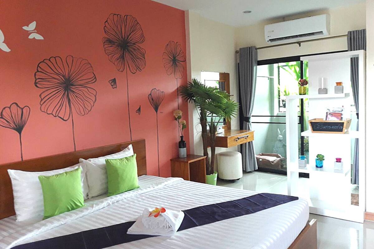 Hotelkamer met een bed, bureau, stoel, een kamerplant en een schuifdeur die leidt naar een balkon.