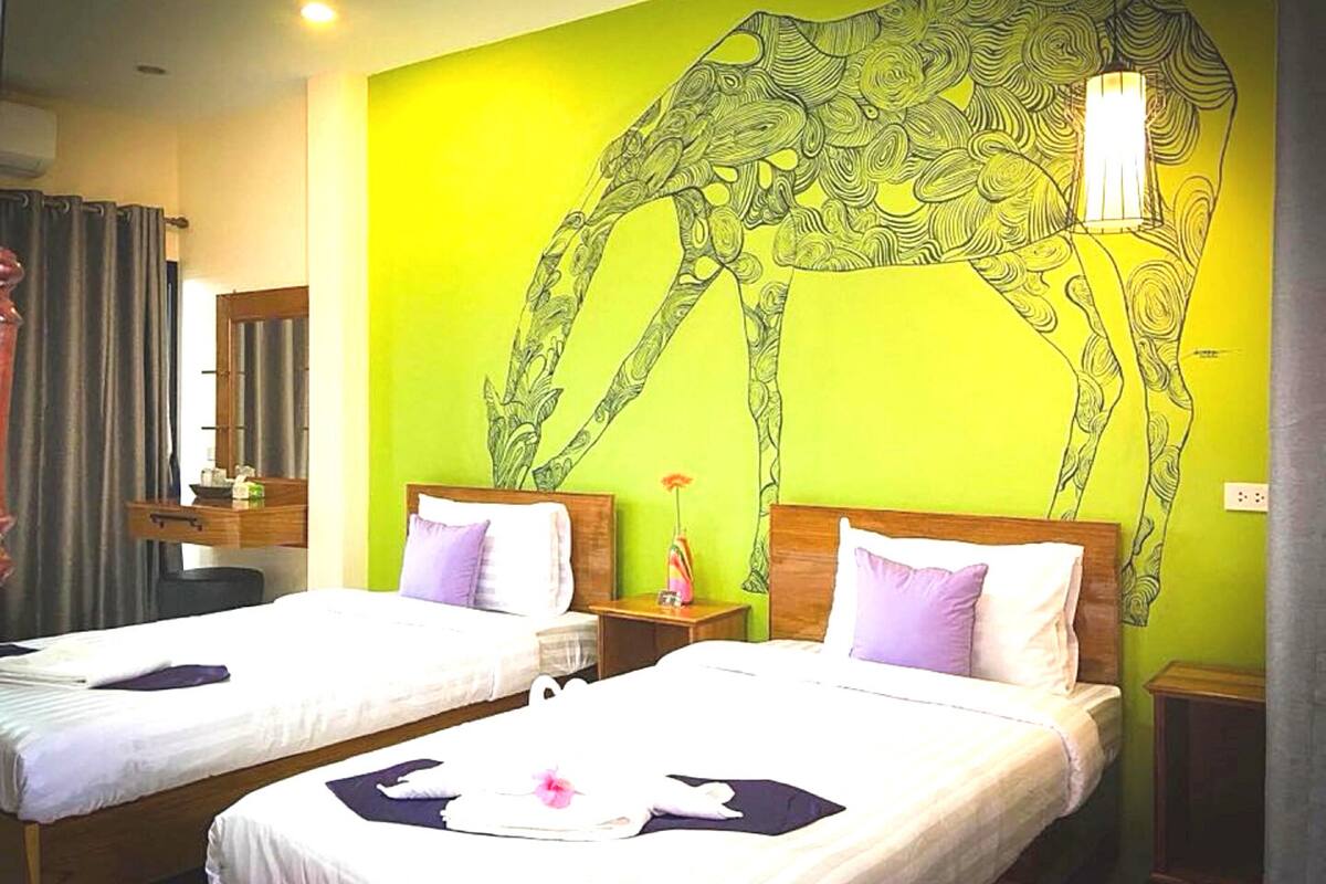 Een hotelkamer met twee bedden, een grote muurschildering van een giraffe en een nachtkastje met een bloemenvaas.