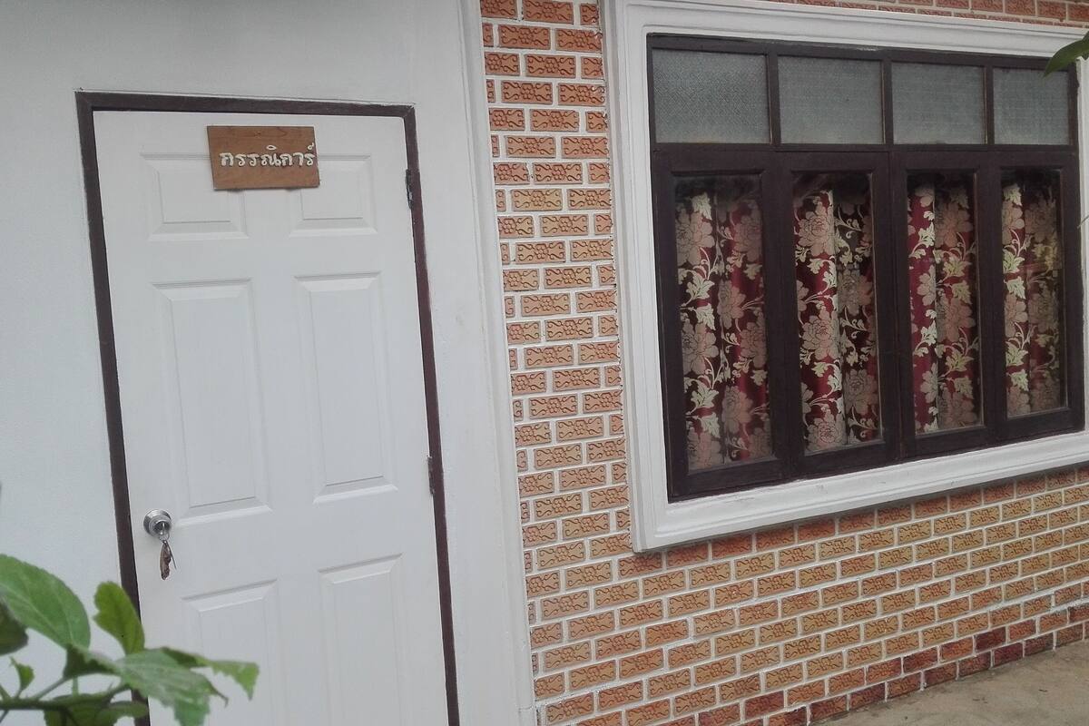 A white door with a sign, a window with floral curtains, and a brick wall.