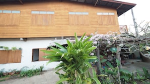 Una casa de madera con techo inclinado, un porche delantero y un jardín con diversas plantas.