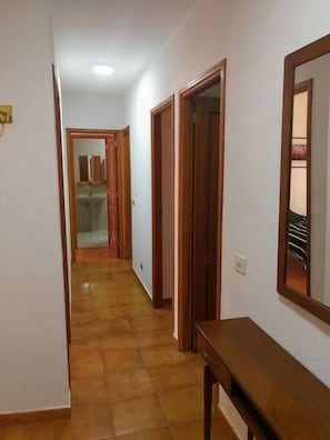 Un couloir avec des portes en bois, un miroir et un sol carrelé.