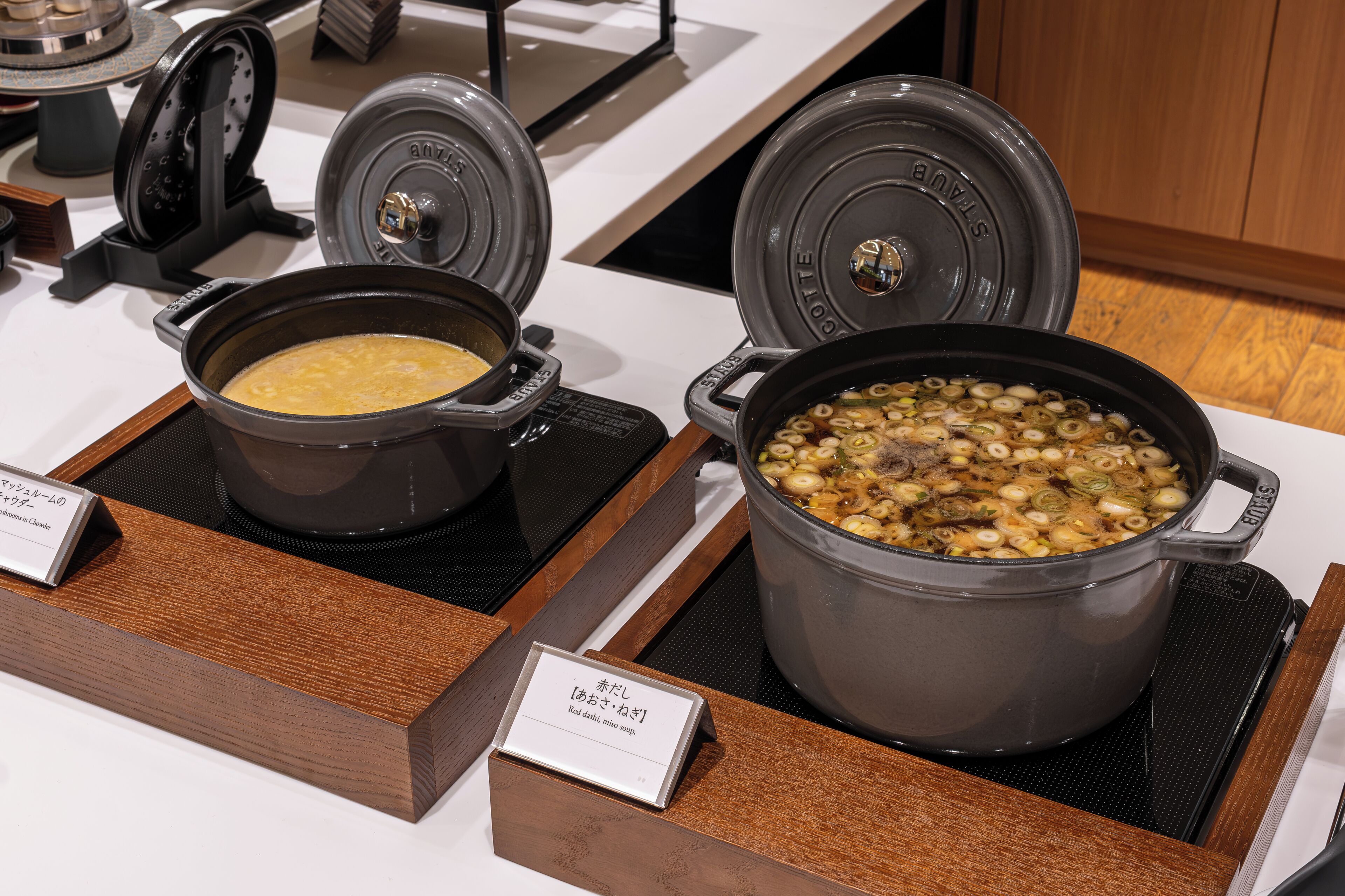 Buffet com dois recipientes: um com sopa amarelada e outro com ensopado de cogumelos e cebolinha.