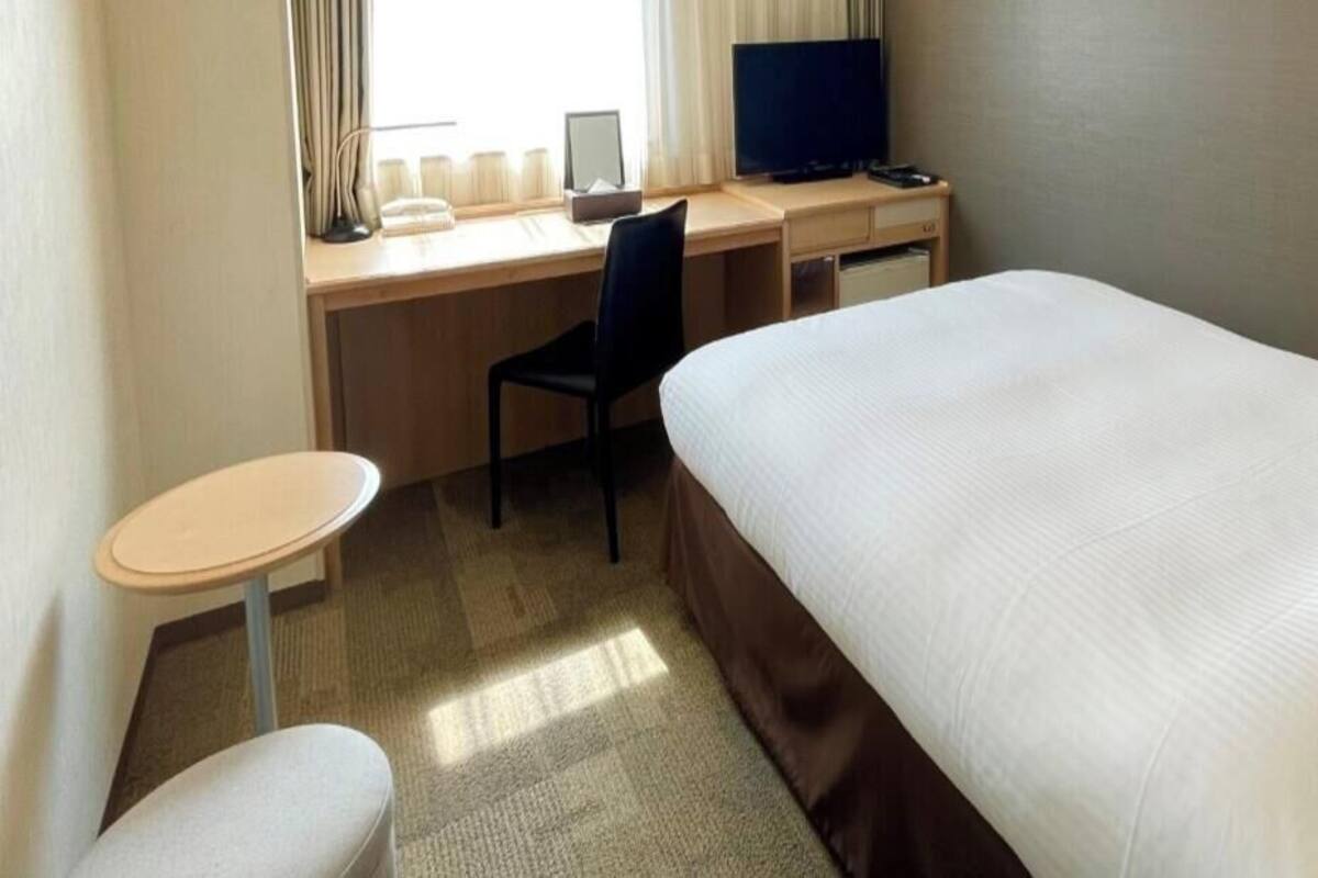 Una habitación de hotel con una cama, un escritorio con una computadora, una silla y una mesita.