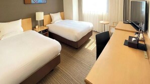 Una habitación de hotel con dos camas, un escritorio, un televisor y una pequeña mesa.