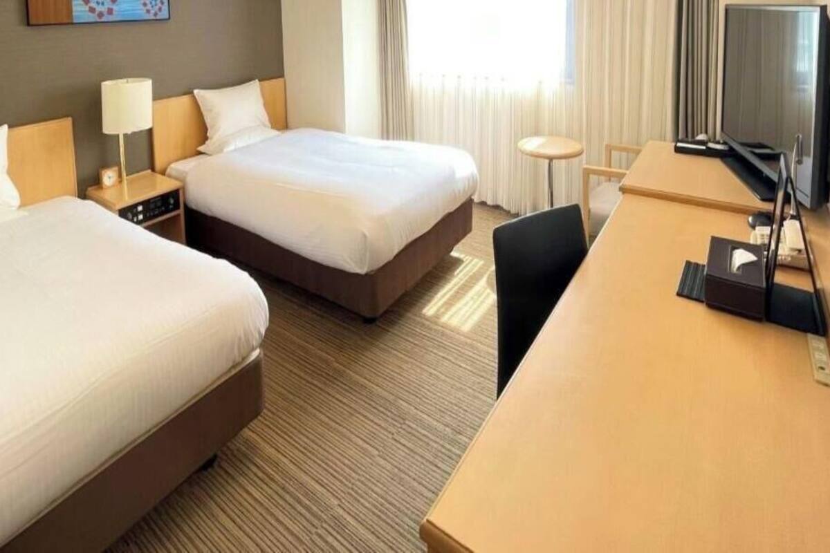 Una habitación de hotel con dos camas, un escritorio, un televisor y una pequeña mesa.