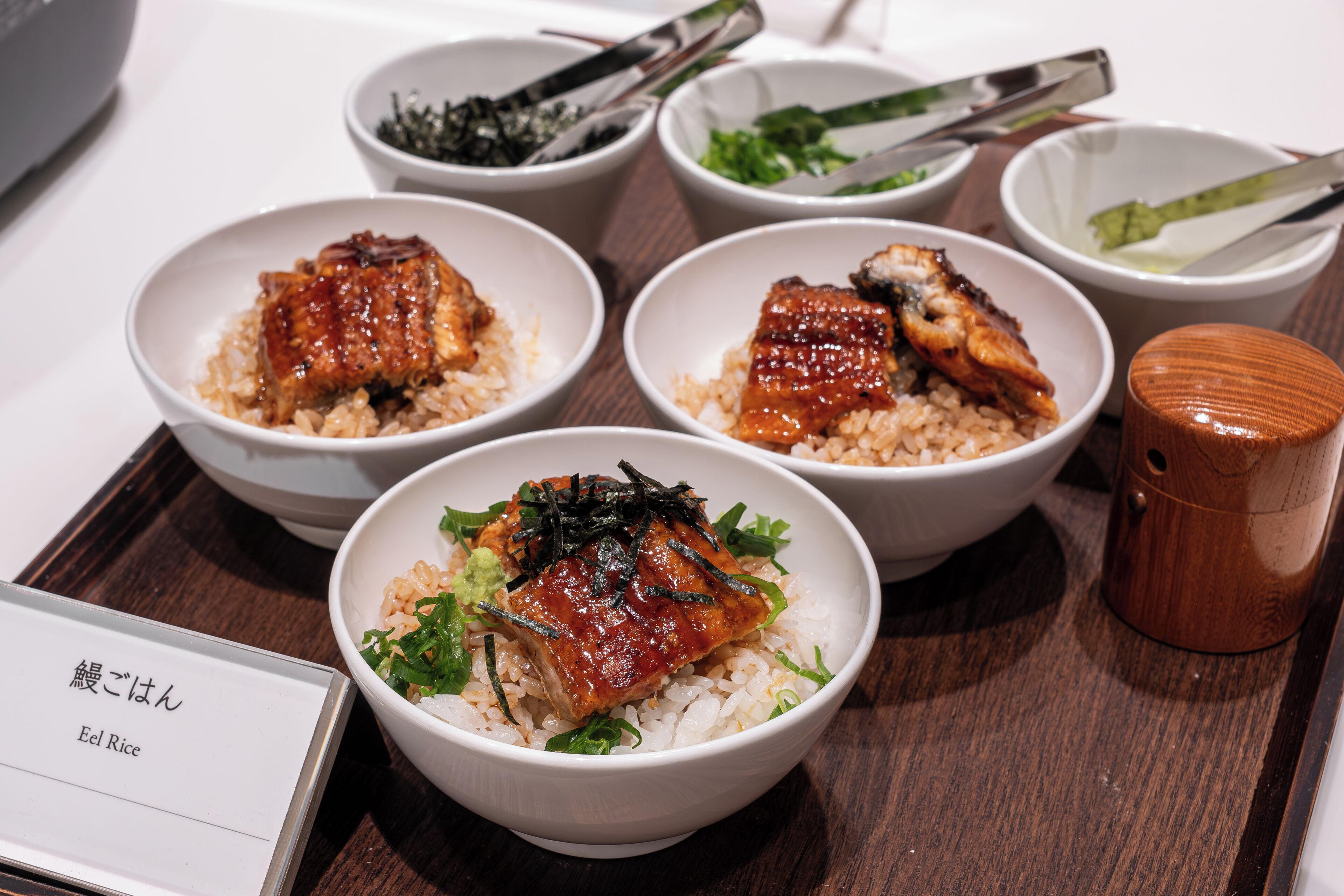 A table with several bowls of rice and fish, accompanied by chopsticks and small dishes of condiments.