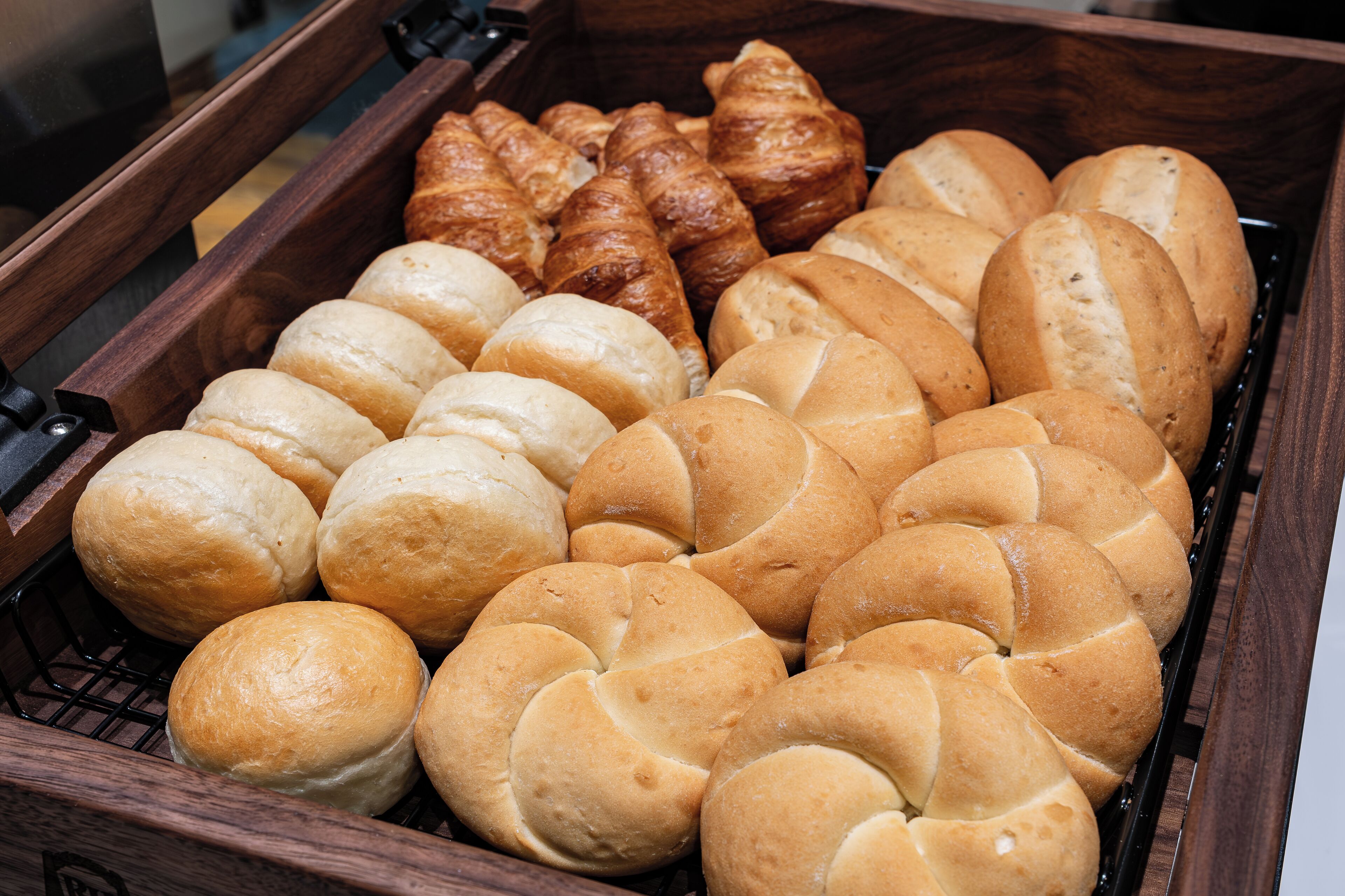 A variety of baked goods including rolls, croissants, and baguettes in a wooden display case.