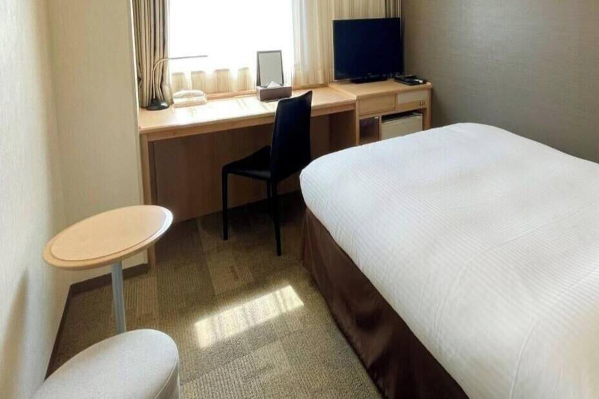 Una habitación de hotel con una cama, un escritorio con una computadora, una silla y una mesita.