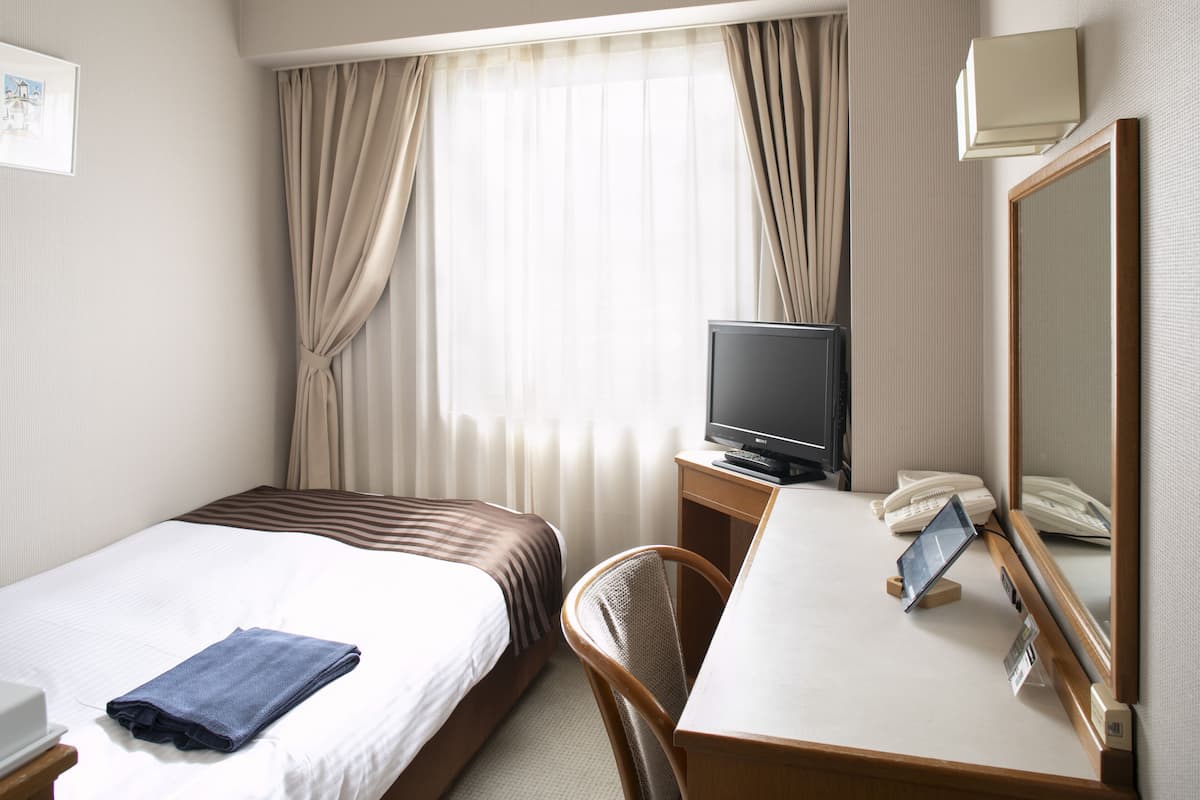 A hotel room with two beds, a desk with a telephone and a television, and a mirror.