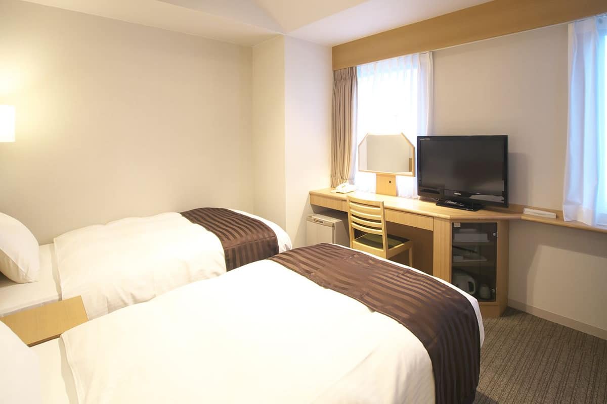 A hotel room with two beds, a desk with a television, and a window with curtains.