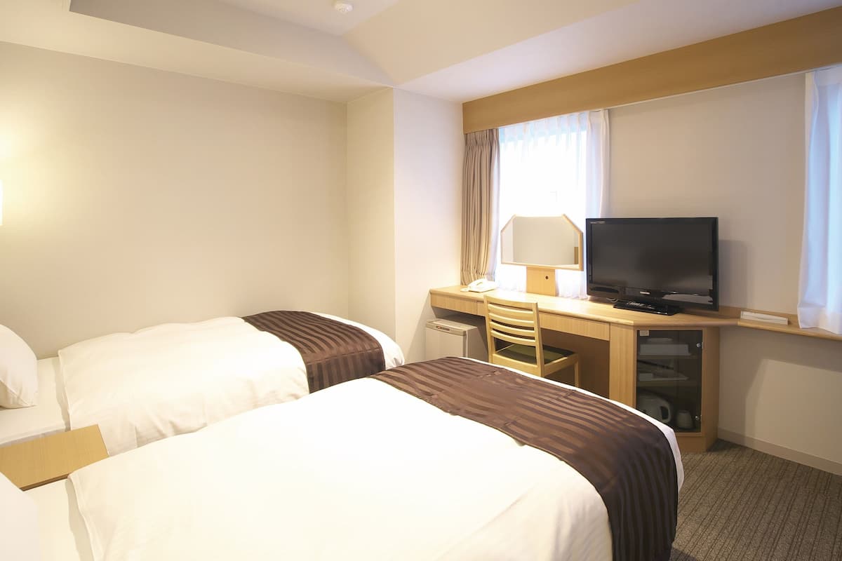 A hotel room with two beds, a desk with a television, and a window with curtains.