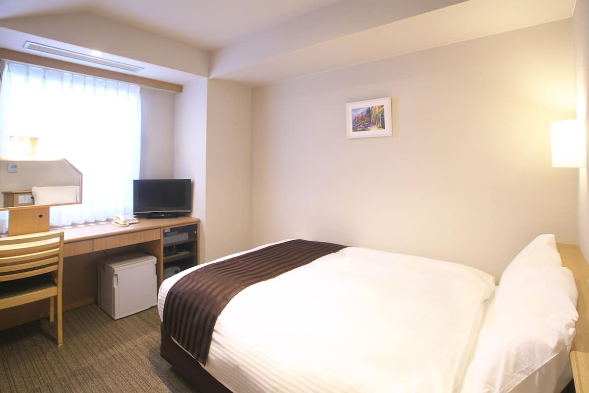 A hotel room with a bed, a desk with a computer, a small refrigerator, and a television.