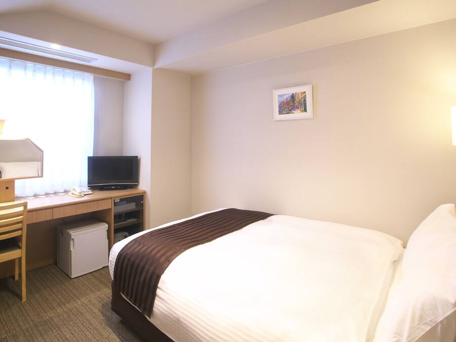 A hotel room with a bed, a desk with a computer, a small refrigerator, and a television.