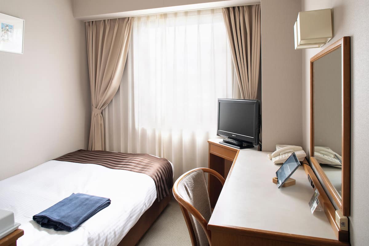 A hotel room with a bed, a desk with a telephone and a small table, a television, and a mirror.