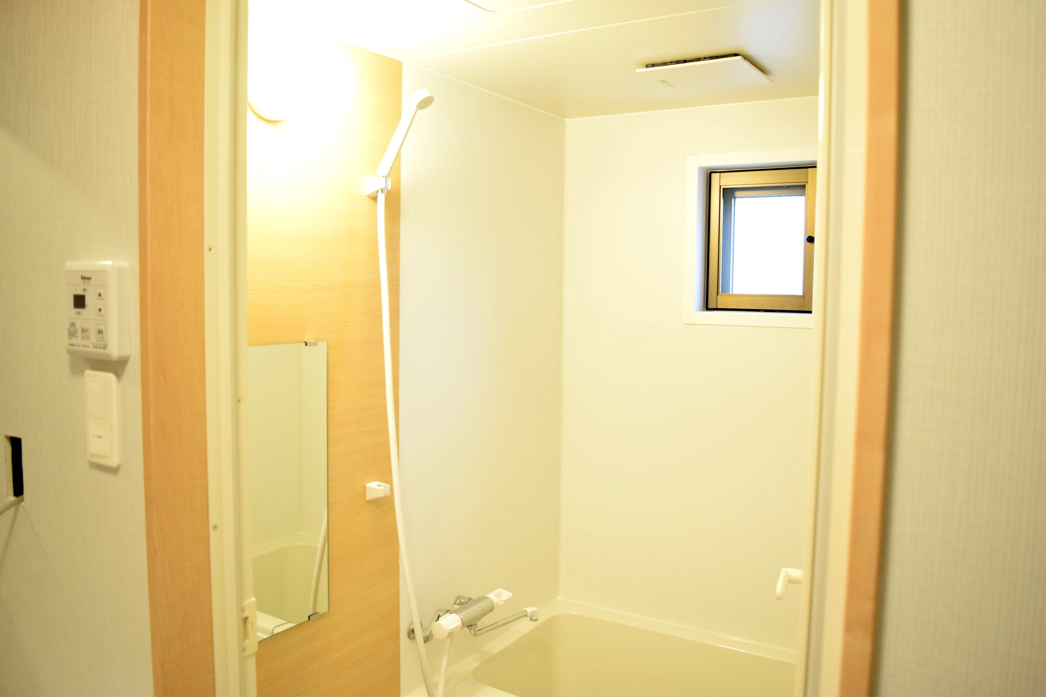 Een badkamer met een douche, een klein raam en een spiegel.