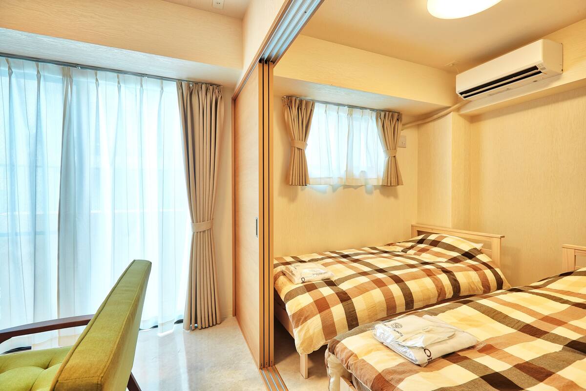 Una camera d'albergo con due letti, una poltrona verde e un condizionatore d'aria.