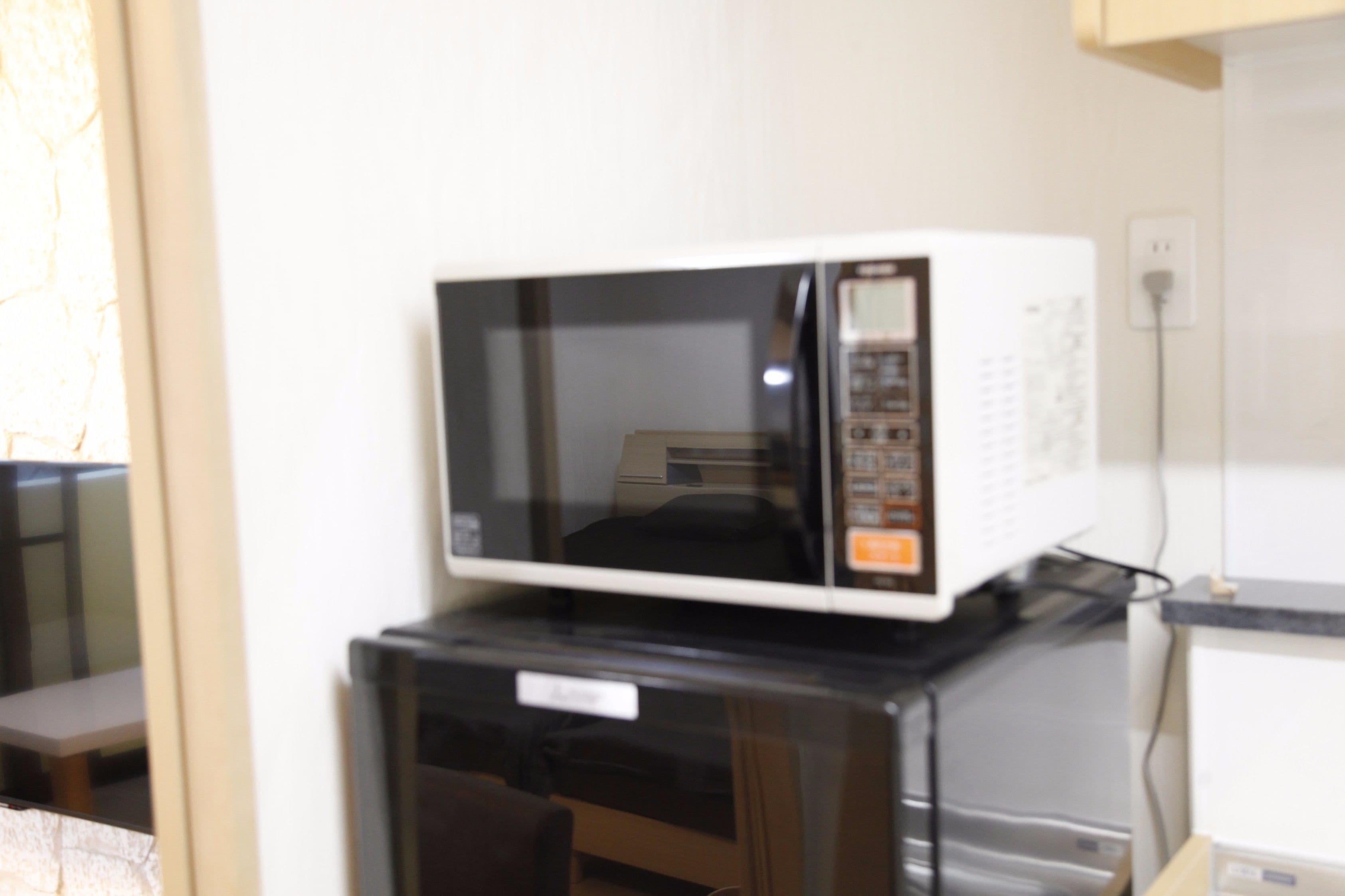 A white microwave on top of a black refrigerator in a kitchen.