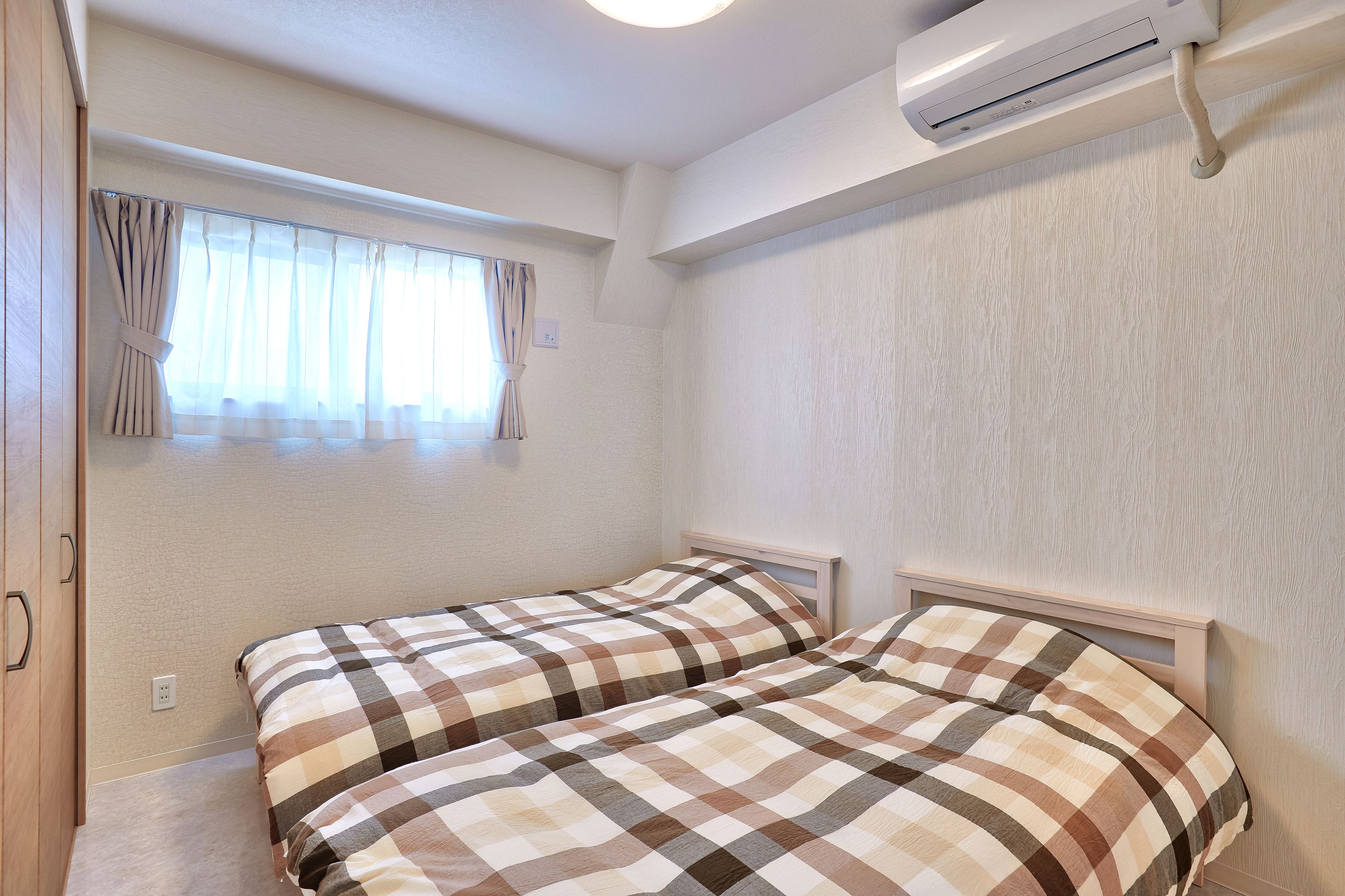 Ein Schlafzimmer mit zwei Betten, einem Fenster mit Vorhängen, einer Klimaanlage und einem Holzschrank.