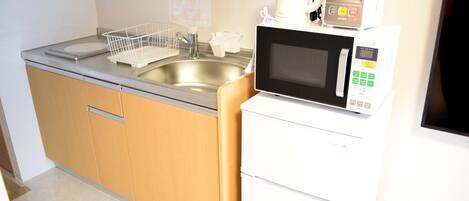 A compact kitchen with a stainless steel sink, a microwave, and a small refrigerator.