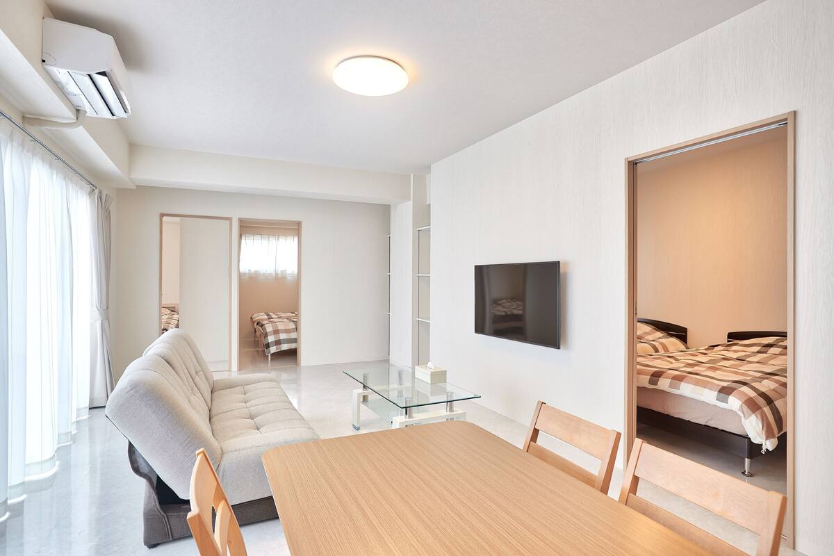 Una moderna camera d'hotel con divano, un tavolino in vetro, un letto con coperta a quadri, una TV a parete e una lampada a soffitto.