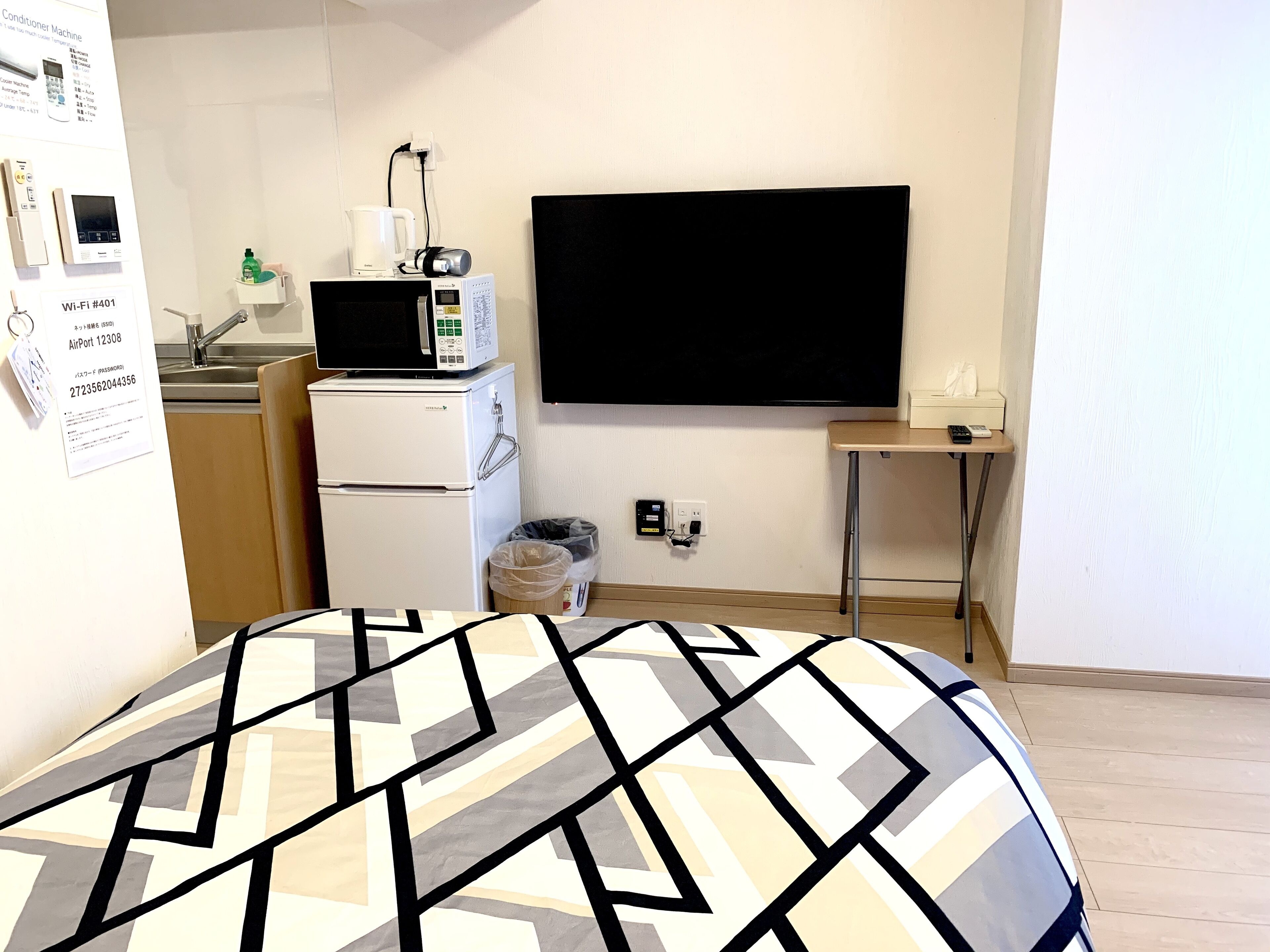 Quarto de hotel compacto com cozinha compacta, televisão de tela plana, uma mesinha e cama com colcha estampada.