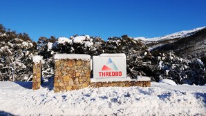 A stone sign with the word "THREDBO" and a logo, surrounded by snow-covered trees and a mountain in the background. - Powder 2a (Thredbo)