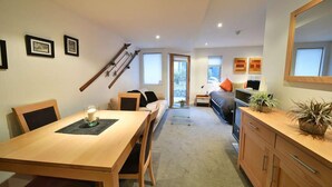 A modern living room with a dining area, a staircase, and a large window. - Powder 2a (Thredbo)