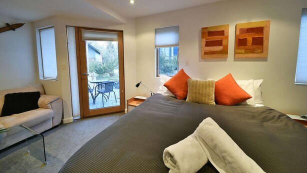 A modern bedroom with a large bed, a sofa, and a sliding glass door leading to an outdoor area. - Powder 2a (Thredbo)