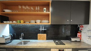 A modern kitchen with a black tiled backsplash, stainless steel appliances, and wooden shelves above the counter. - Powder 2a (Thredbo)