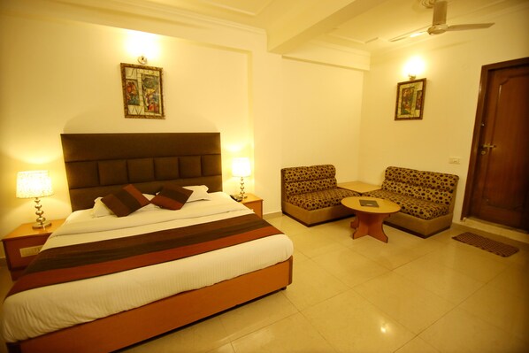 A hotel room with a large bed, two armchairs, a small round table, and a ceiling fan.