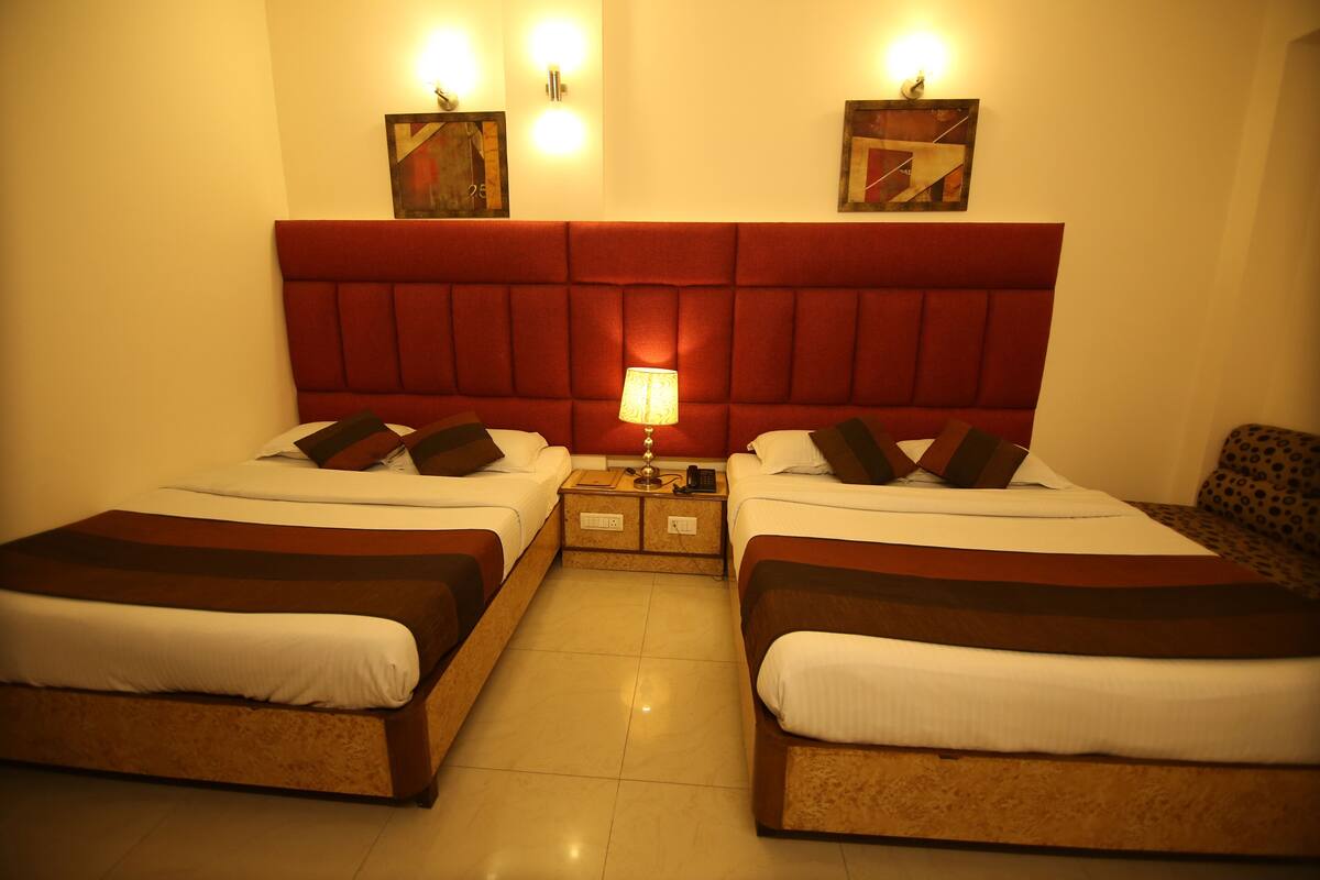 Habitación de hotel con dos camas, un cabecero rojo, una mesita de noche con lámpara y obras de arte en las paredes.