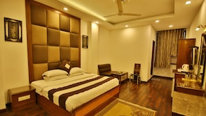 A hotel room with a large bed, a desk, a chair, a wardrobe, and a ceiling fan. - Hotel Parkway Deluxe (New Delhi)