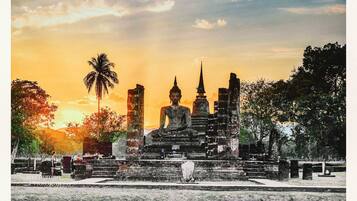 Ein Tempelkomplex mit mehreren Buddha-Statuen, einer großen zentralen Statue und einer Palme.