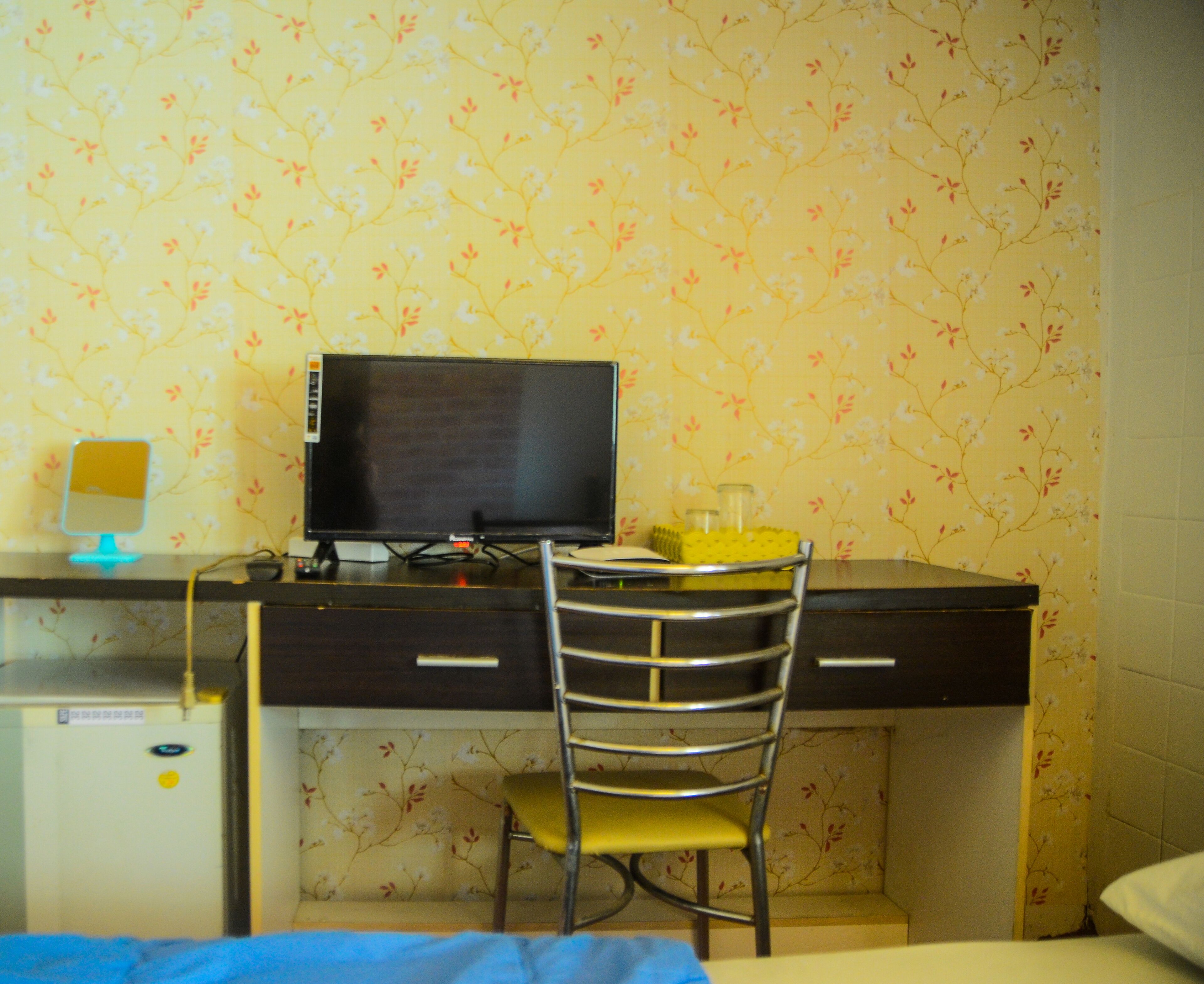 Une petite pièce comprenant un bureau, une chaise, un téléviseur et un lit.