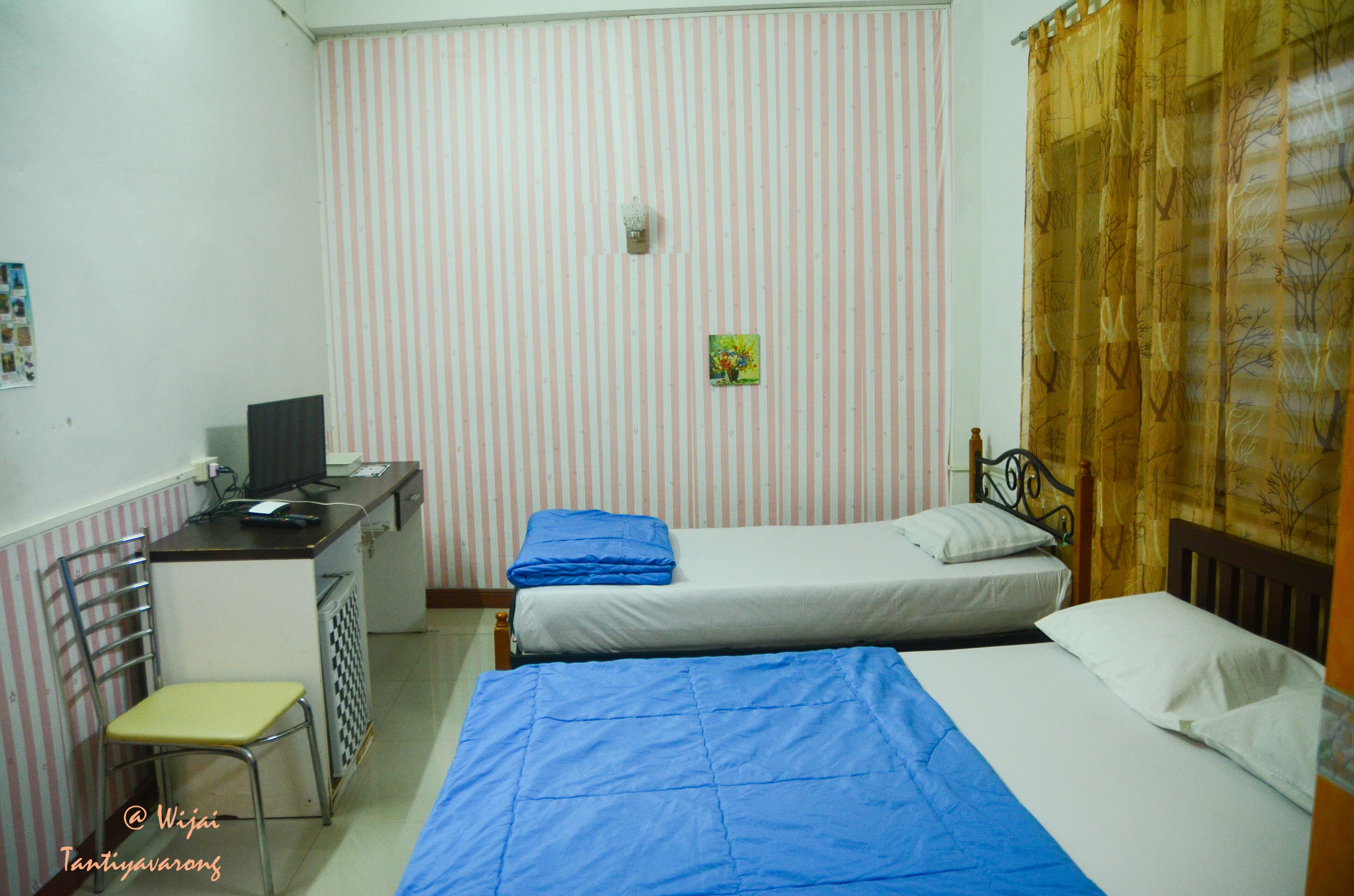 A small, compact room with two single beds, a desk with a computer, and a chair.