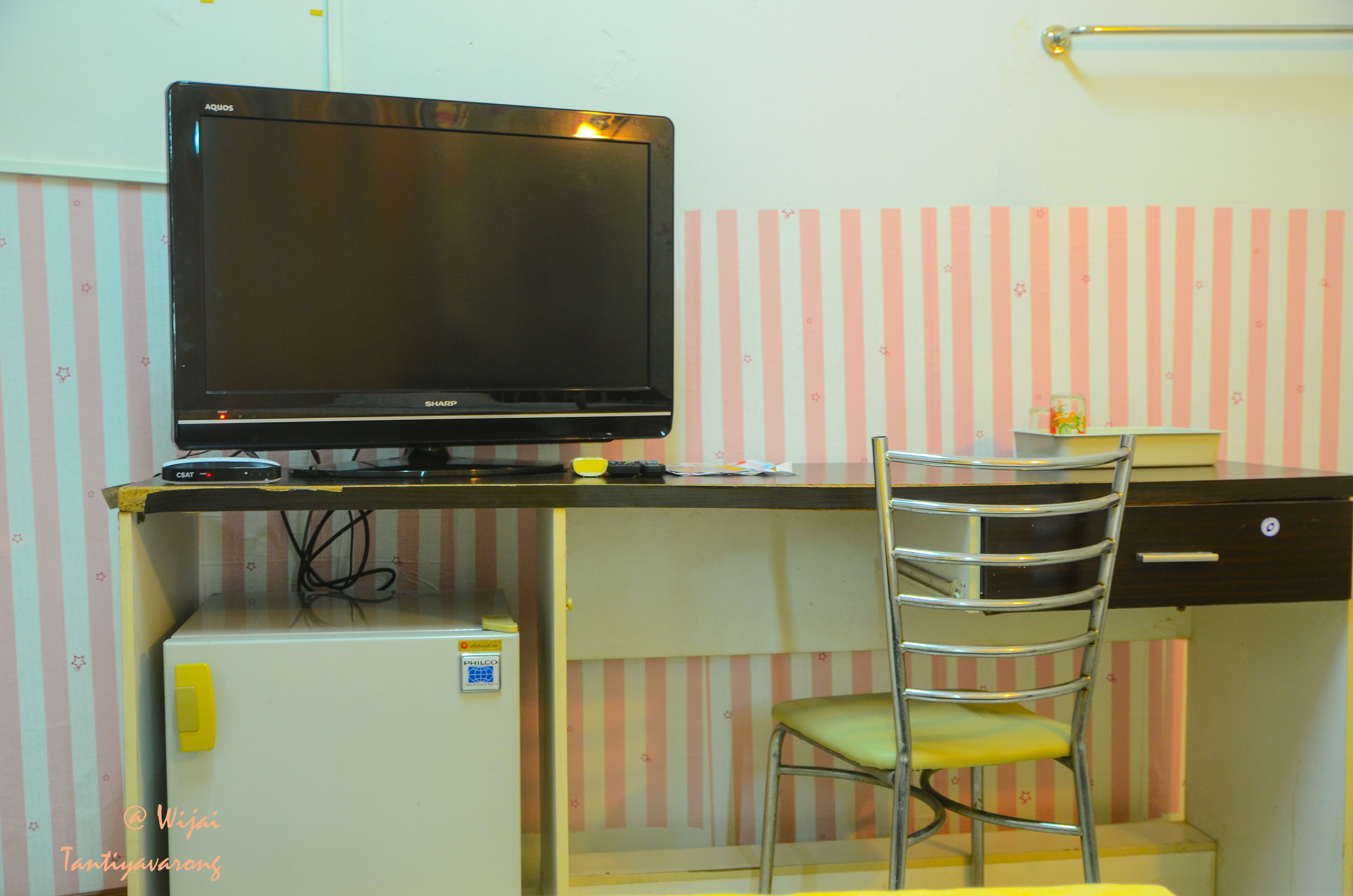 Un espacio de trabajo funcional con un televisor sobre un escritorio, una silla y un refrigerador pequeño.