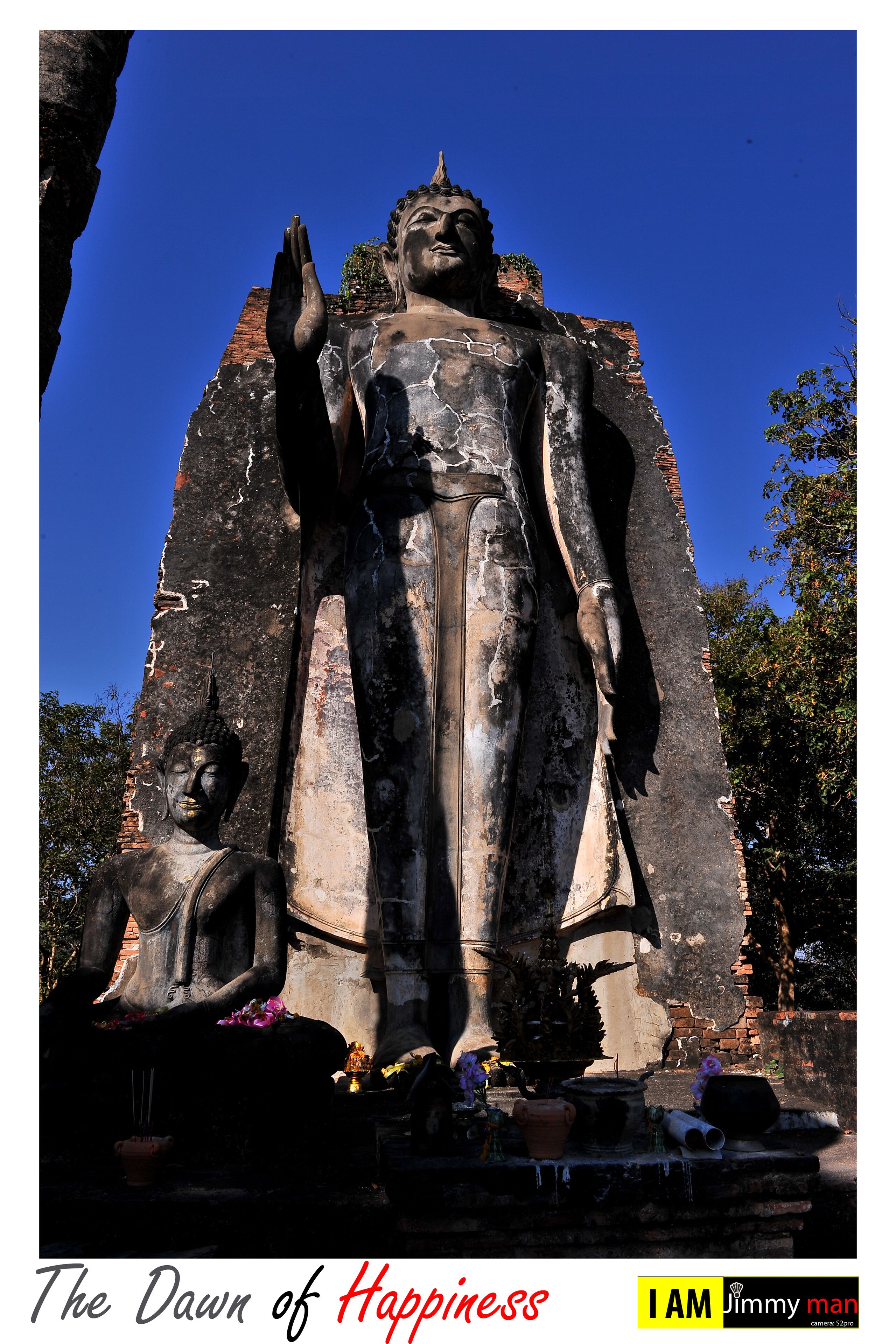 A large Buddha statue with a smaller statue beside it, both set against a clear blue sky.